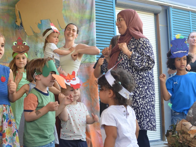 Kinder und Erwachsene bewegen sich gemeinsam bei der Sommerfest-Aufführung; mehrere Kinder tragen selbst gebastelte Tiermasken.