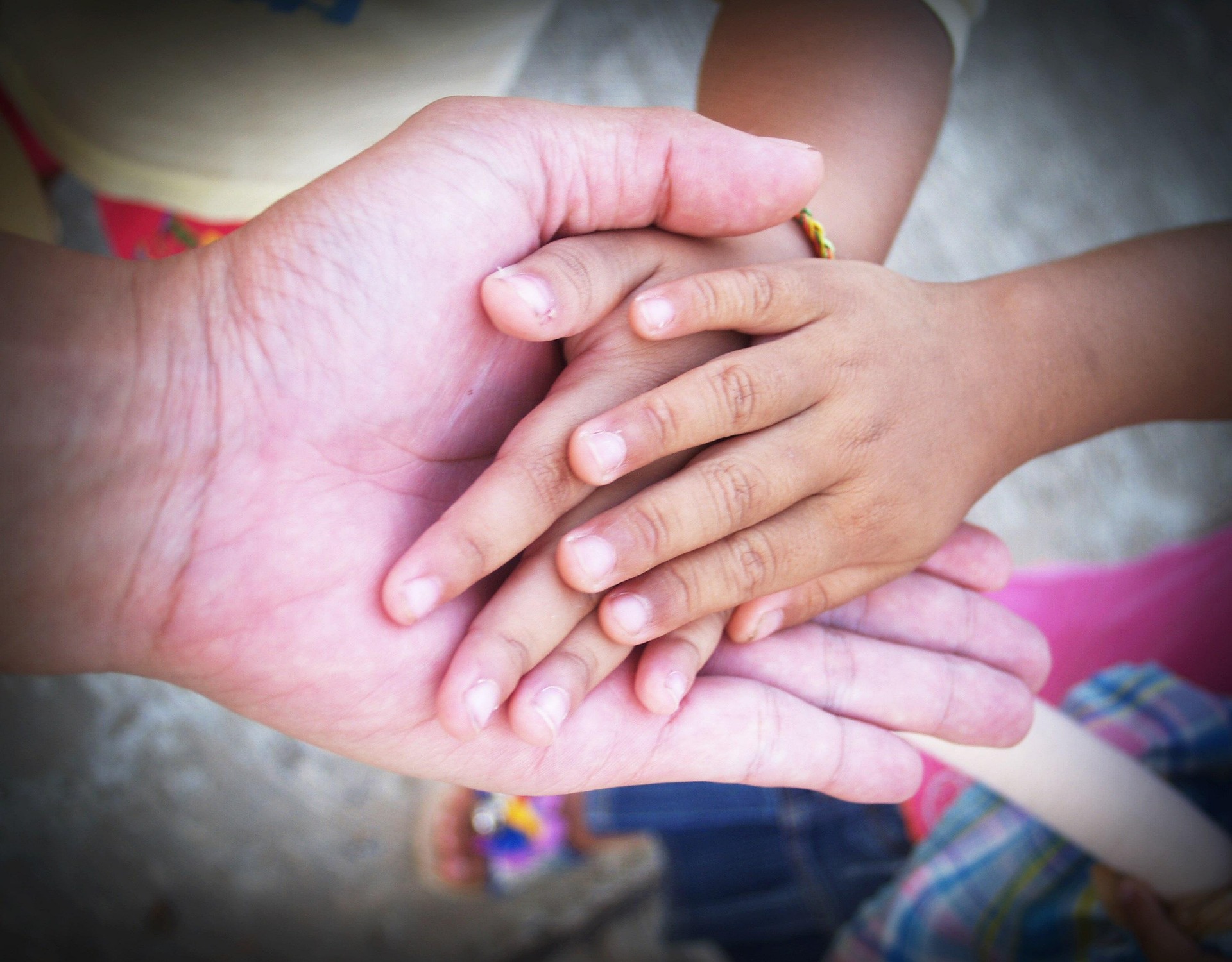 Mehrere Kinderhände liegen gemeinsam in den geöffneten Händen einer erwachsenen Person.