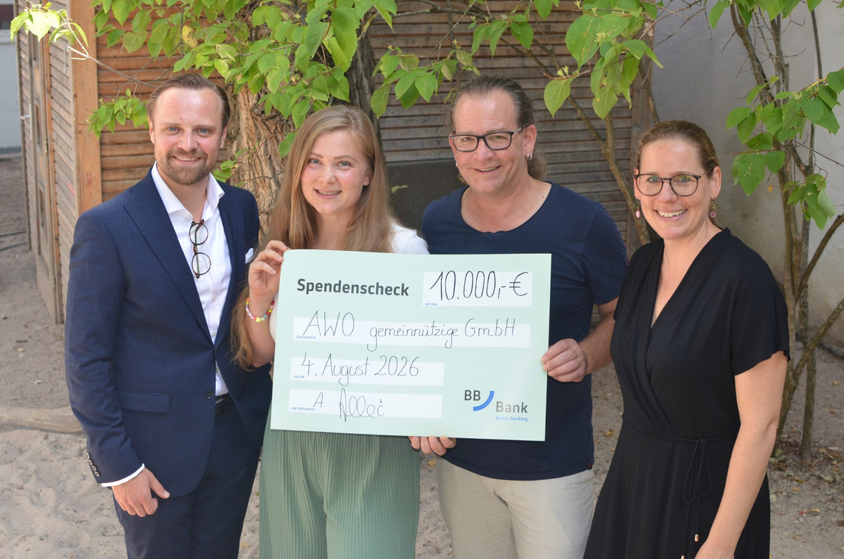 Vier Personen stehen im Freien und halten gemeinsam einen symbolischen Spendenscheck der BBBank über 10.000 Euro für die AWO Karlsruhe.