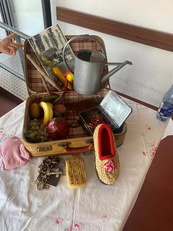 Historische Alltagsgegenstände wie eine Gießkanne, Schuhe und Obst liegen auf einem Tisch.