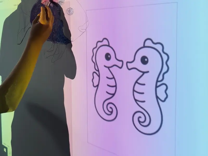 Eine Person überträgt die Kontur zweier Seepferdchen mithilfe eines Projektors auf eine Wand.
