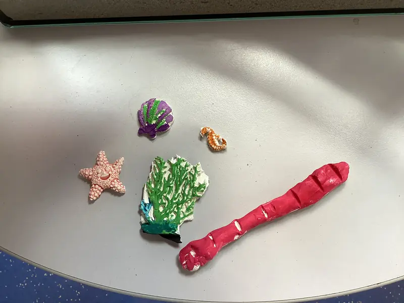 Mehrere kleine Meerestiere aus bemalter Modelliermasse liegen auf einem Tisch.