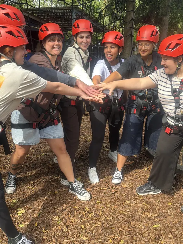 Mitarbeitende der Kita Mikado stehen mit roten Kletterhelmen zusammen und legen ihre Hände in die Mitte.