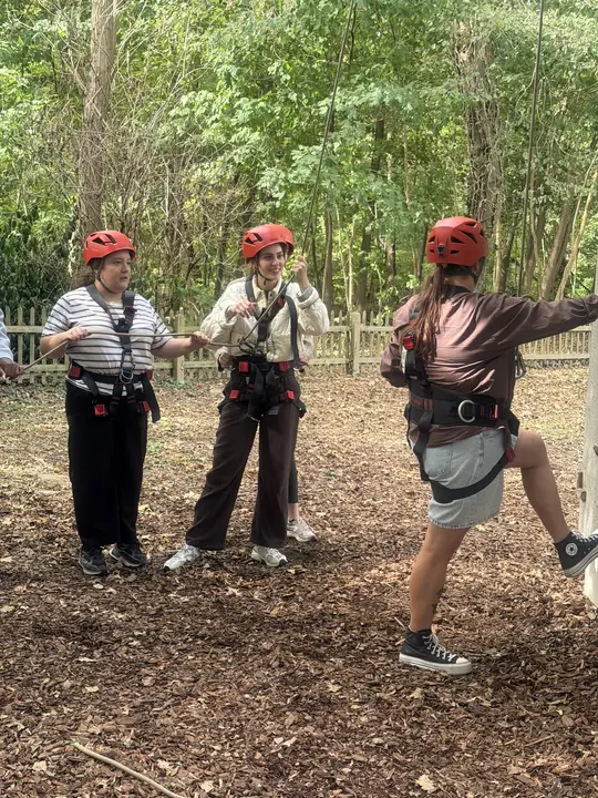 Drei Mitarbeitende der Kita Mikado stehen mit Kletterhelmen und Gurten im Wald