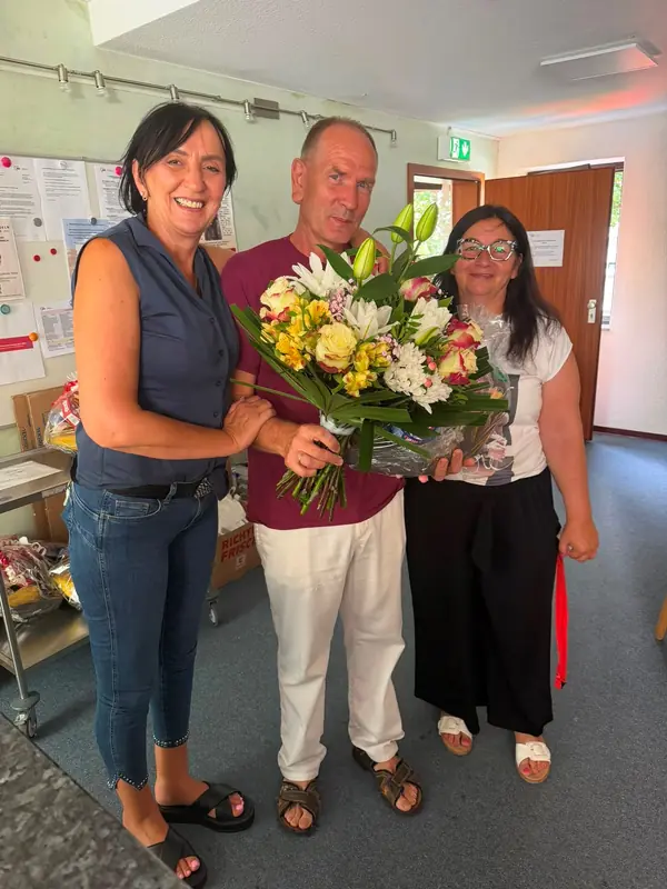 Oleg Weimert, Anke Agsten und Mirjana Braitsch stehen gemeinsam mit einem Blumenstrauß im Flur.