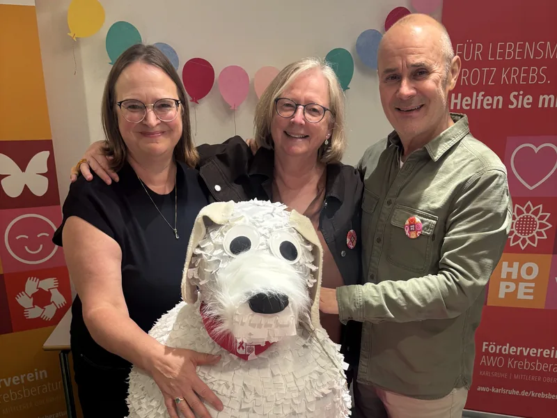 Franziska Petridis, Antje Göbel und Ertürk Bayram stehen hinter einer großen weißen Hunde-Piñata mit rotem Halstuch.