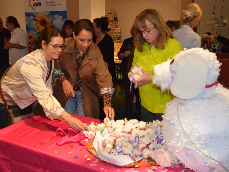 Drei Frauen betrachten und nehmen kleine weiße HOPE-Plüschhunde von einem Tisch neben der großen Hunde-Piñata.