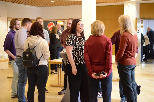 Mehrere Teilnehmende der Kreiskonferenz stehen in einem hellen Foyer im Gespräch. Eine Frau im schwarz-weißen Musterkleid steht mittig in der Gruppe.