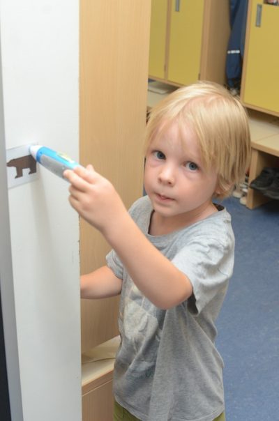 Ein Kind hält ein kleines elektronisches Gerät an ein Symbol an der Wand.