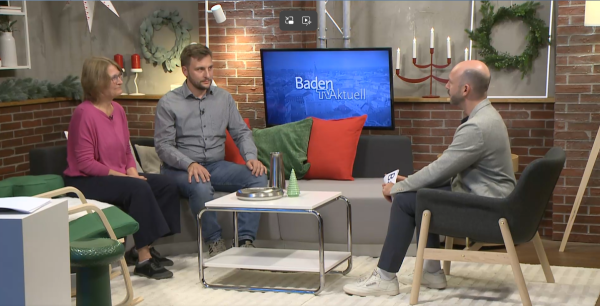 Screenshot aus der Sendung „Baden TV aktuell“: Karen Eßrich und Oliver Hill sitzen im Studio im Gespräch mit einem Moderator.