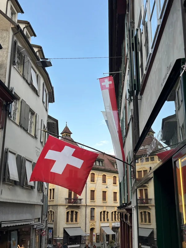 Schweizer Flaggen hängen über einer Gasse mit historischen Häusern in Basel.