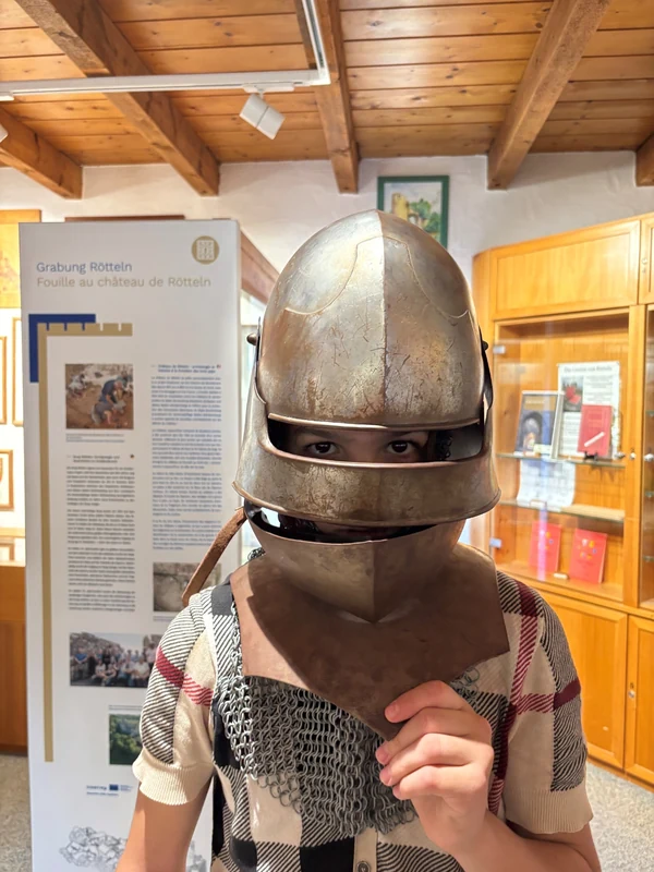 Eine Person probiert in einem Innenraum große mittelalterliche Panzerhandschuhe an.